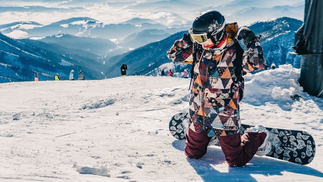 A snowboarder kneeling at the top of a ski mountain. 