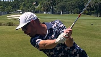 A man swings a golf club on a golf course.