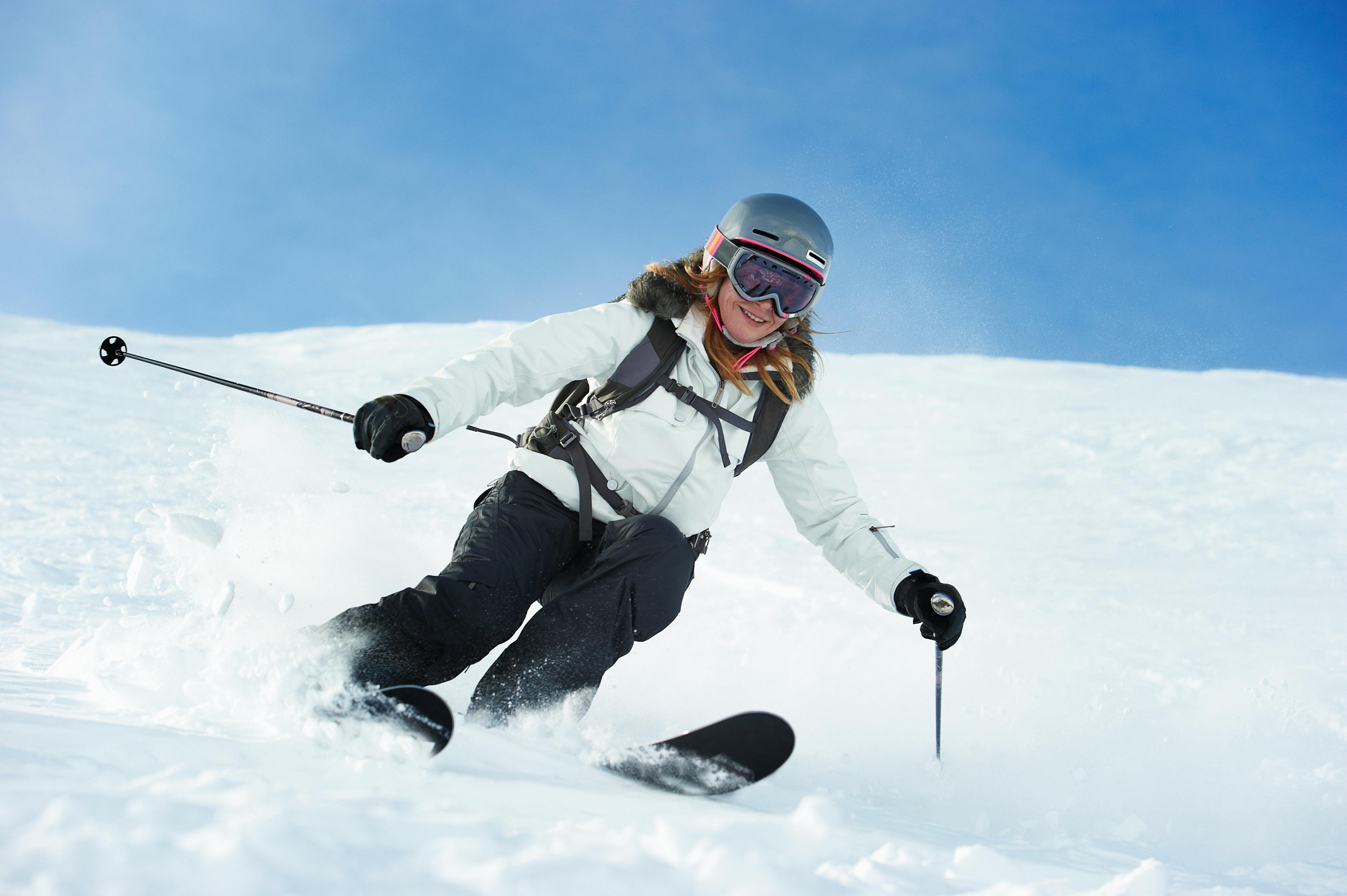 A woman in a white jacket and black pants smiles as she skis