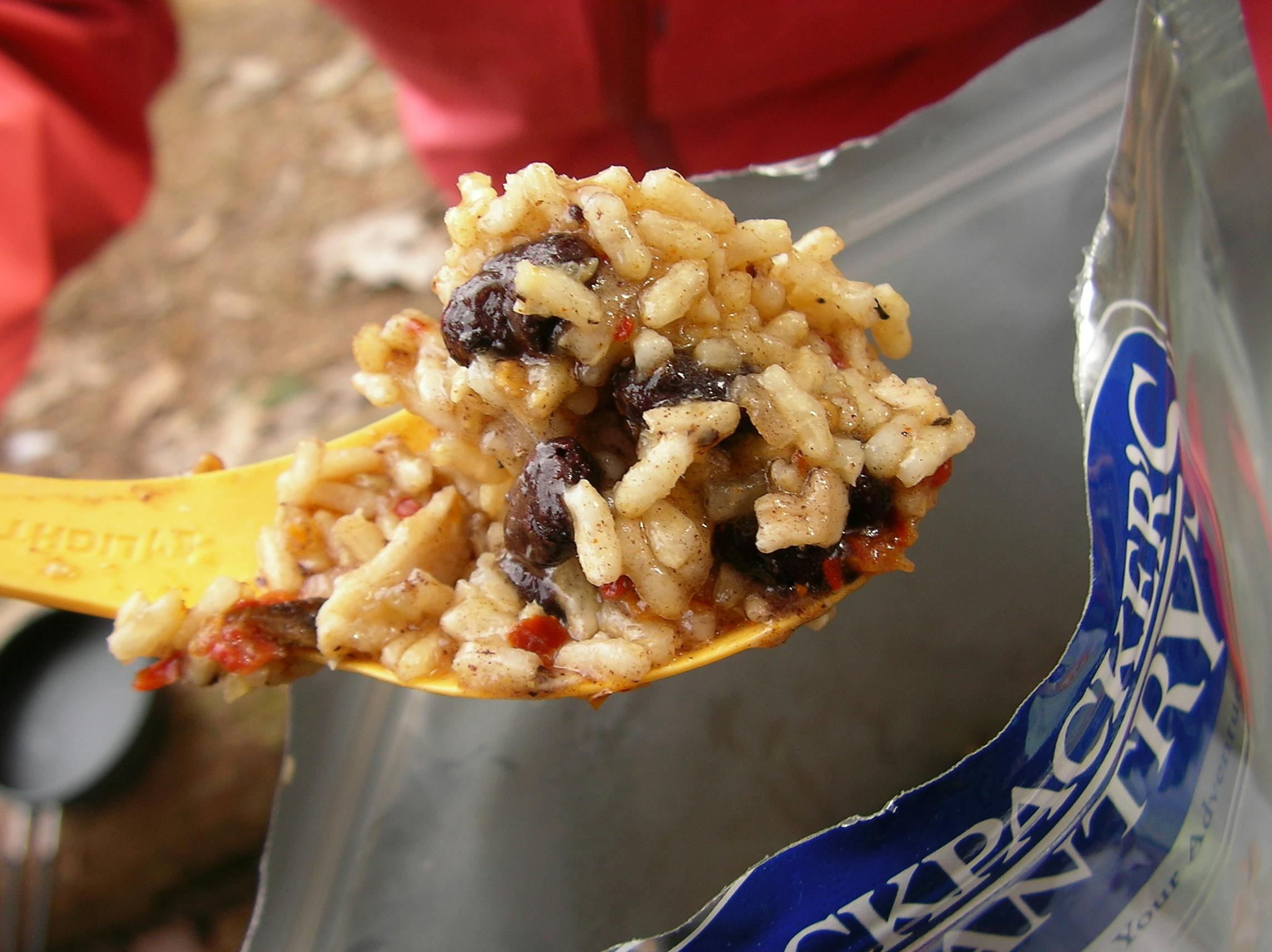 A spoon with food on it. The food is coming from a container of a Backpackers Pantry meal.