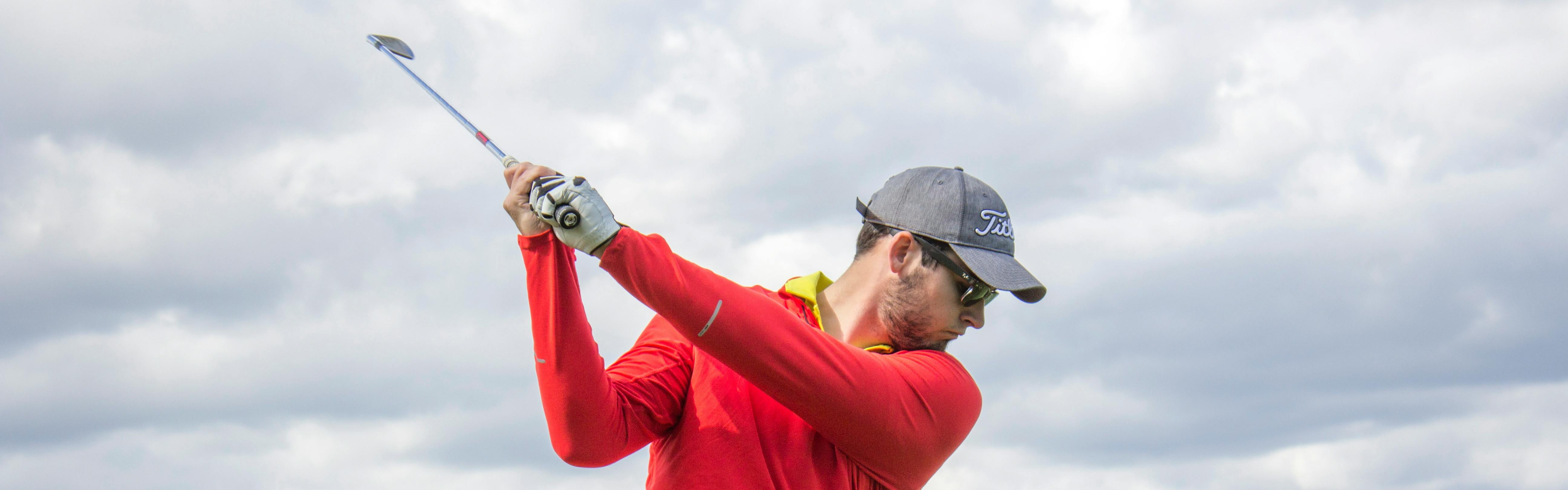 A closeup on a golfer in a red long-sleeved shirt in the midst of a golf swing