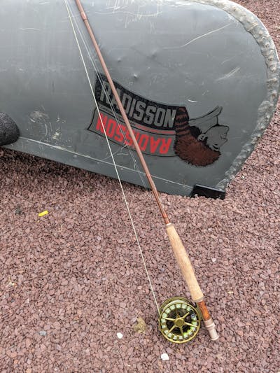 The The Lamson Guru S Fly Reel and a fishing rod propped up against a canoe.