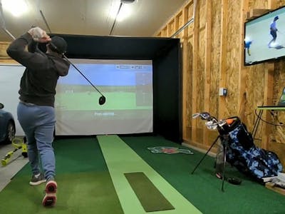 A man takes a swing with a golf club in a simulator.
