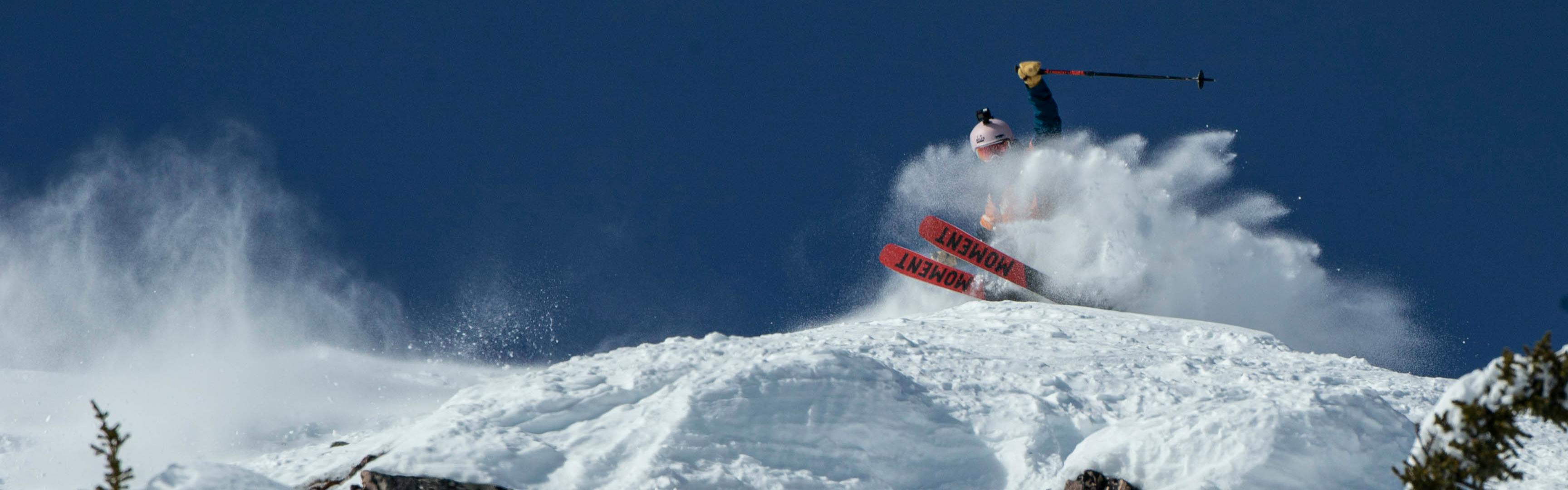 A skier carves a turn on a lip, sending up a cloud of powder with their Moment skis. 