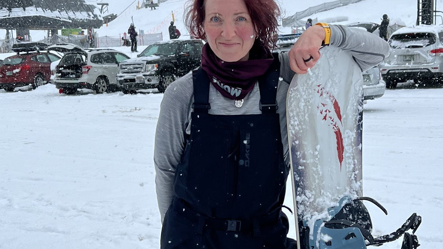 A snowboarder standing with her snowboard in the Dakine Women's Reach 20K Bibs.