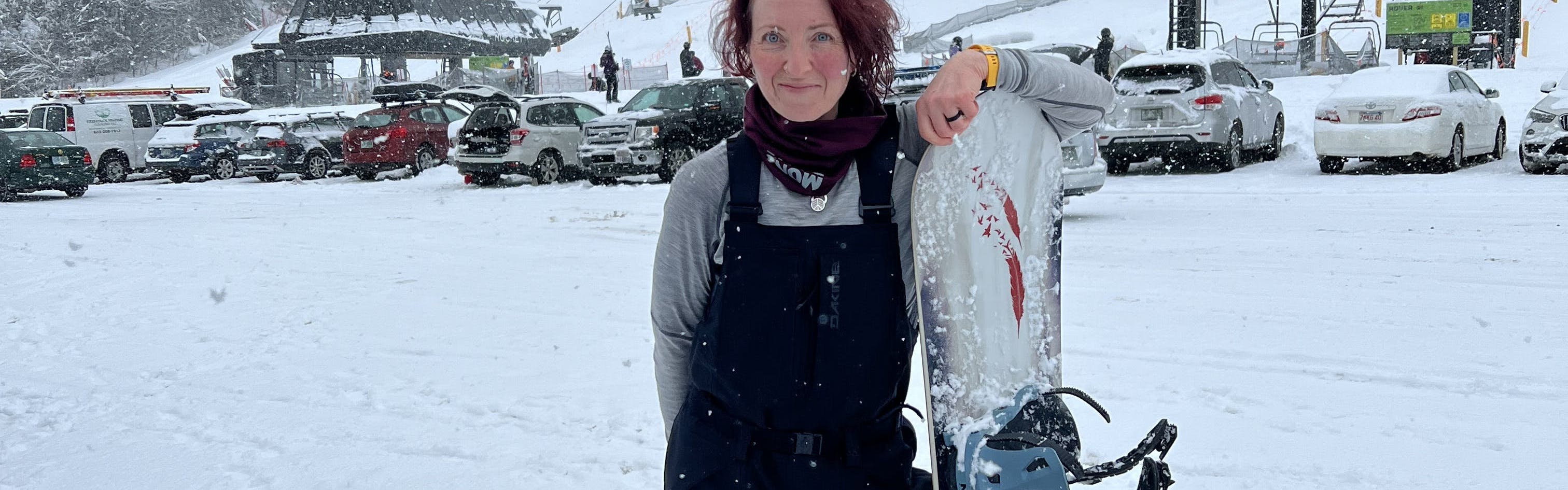 A snowboarder standing with her snowboard in the Dakine Women's Reach 20K Bibs.