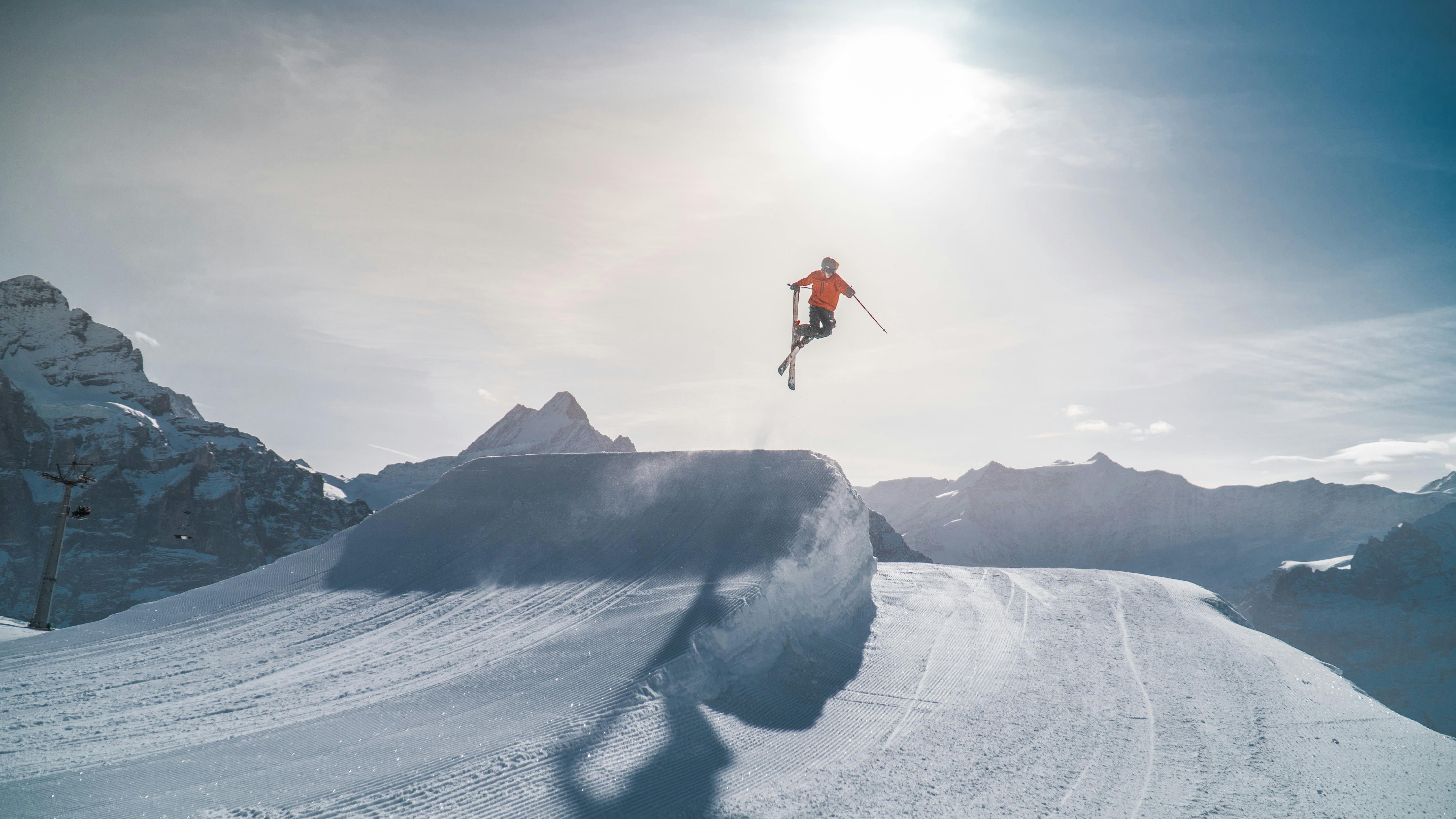 A skier in an orange jacket crosses their skis behind them as they execute a jump