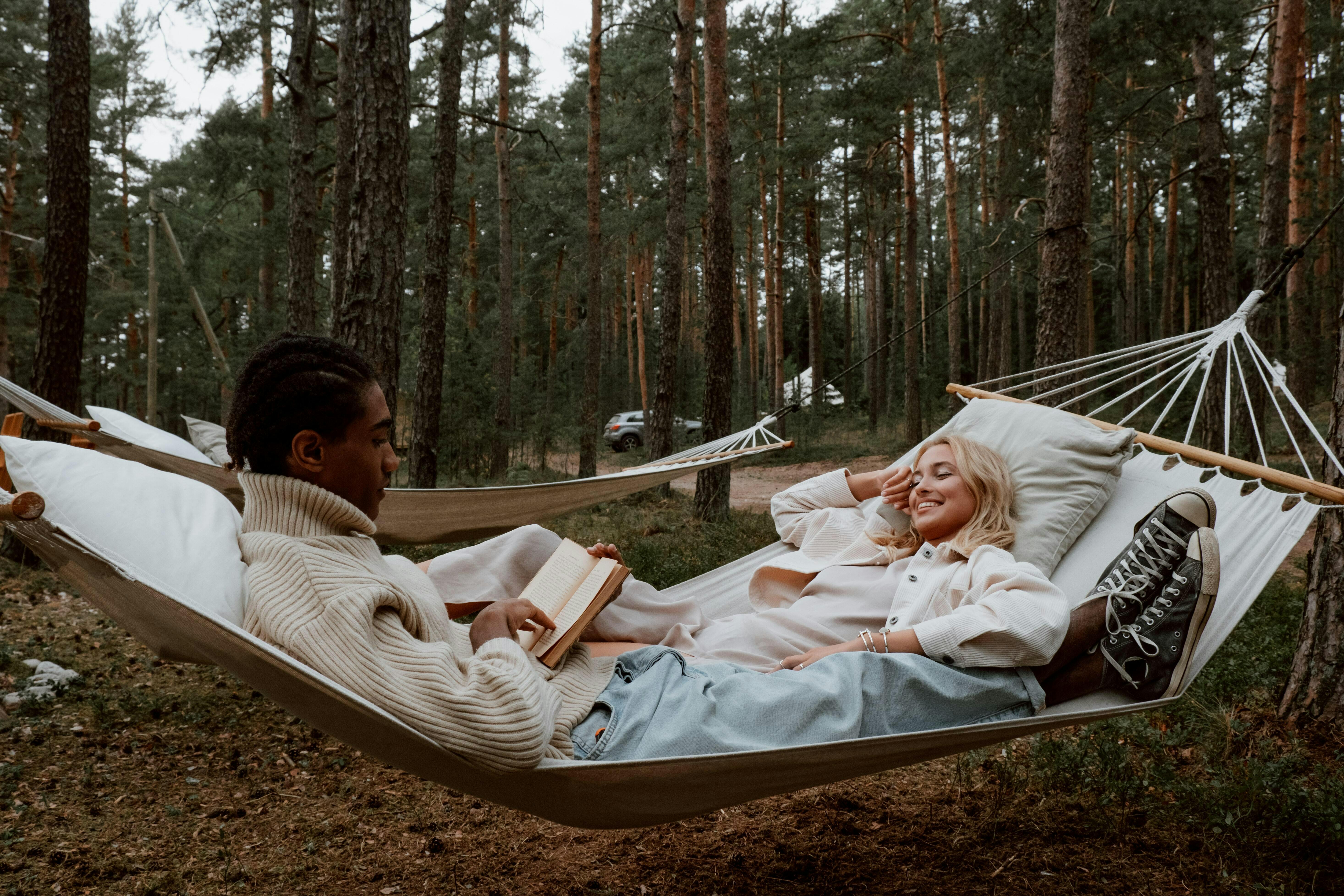 Two people in a hammock. One is reading a book and one is laughing.