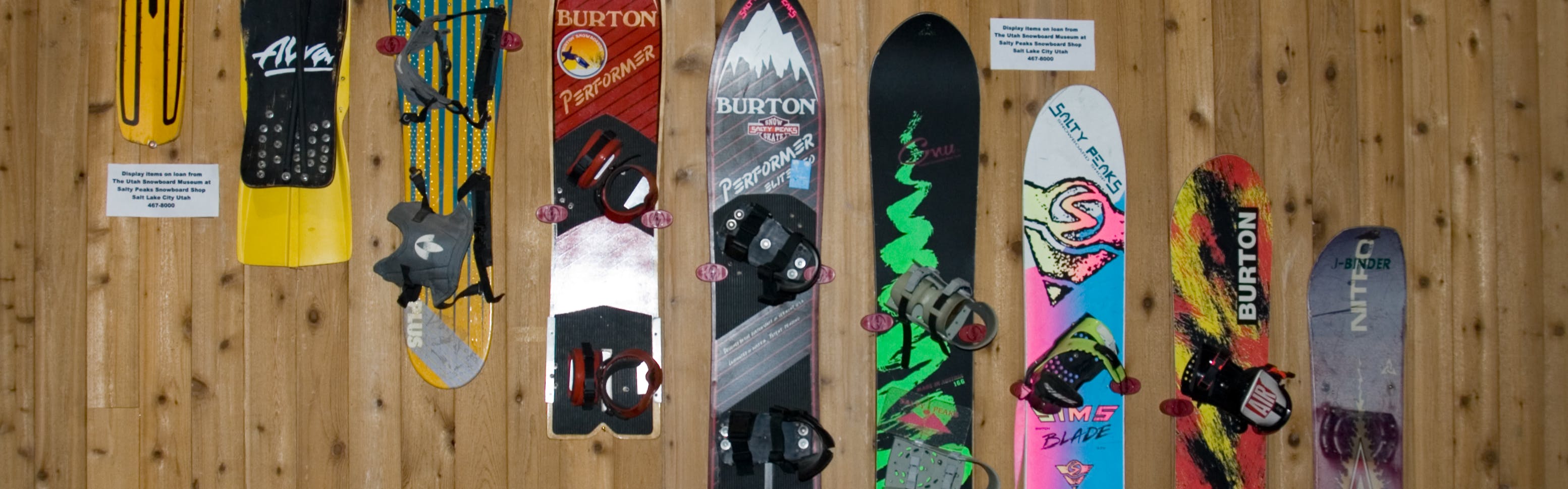 Several generations of snowboards hanging on a wall. 