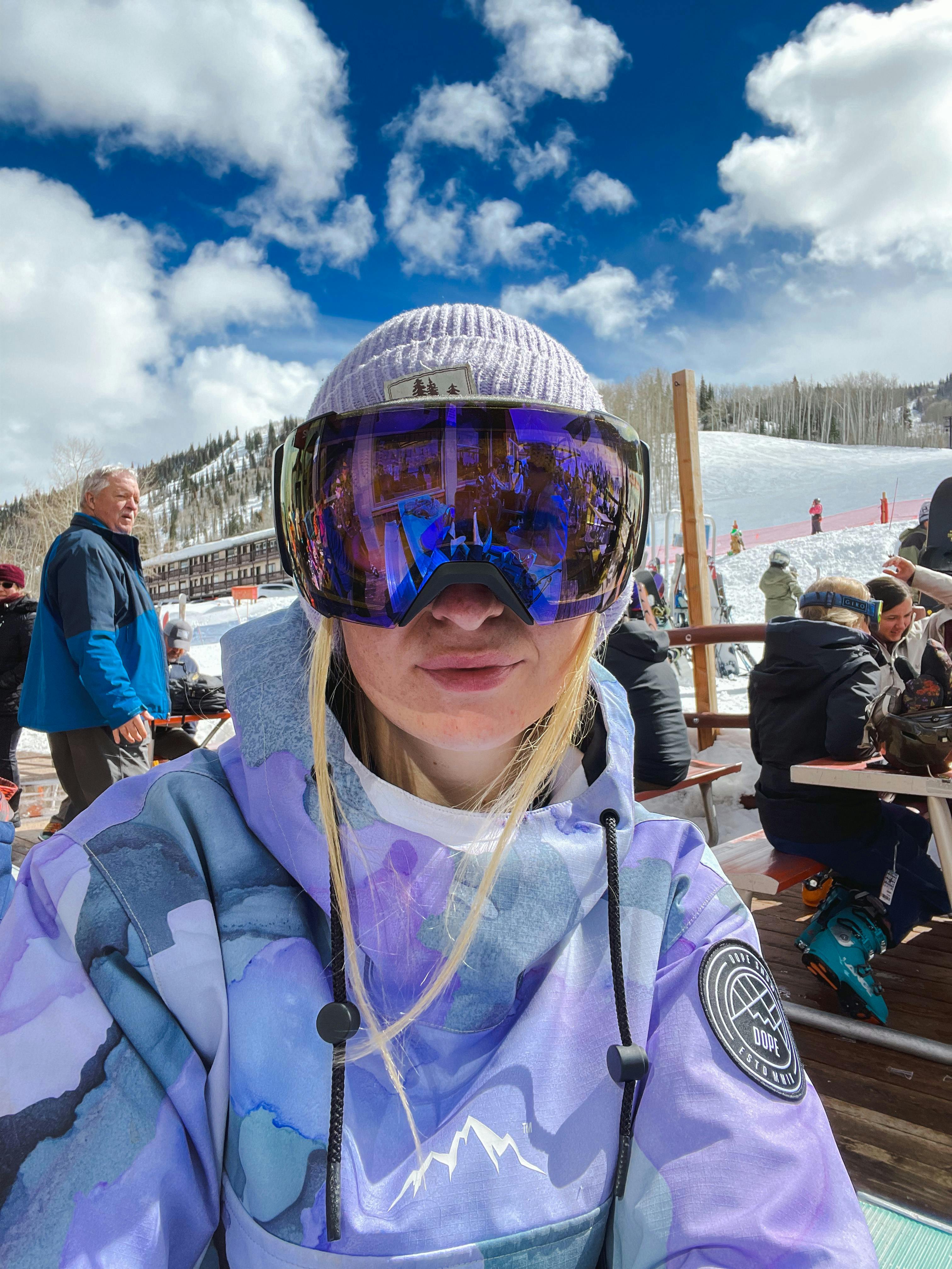 A person in goggles sitting at the base area of a ski area. 