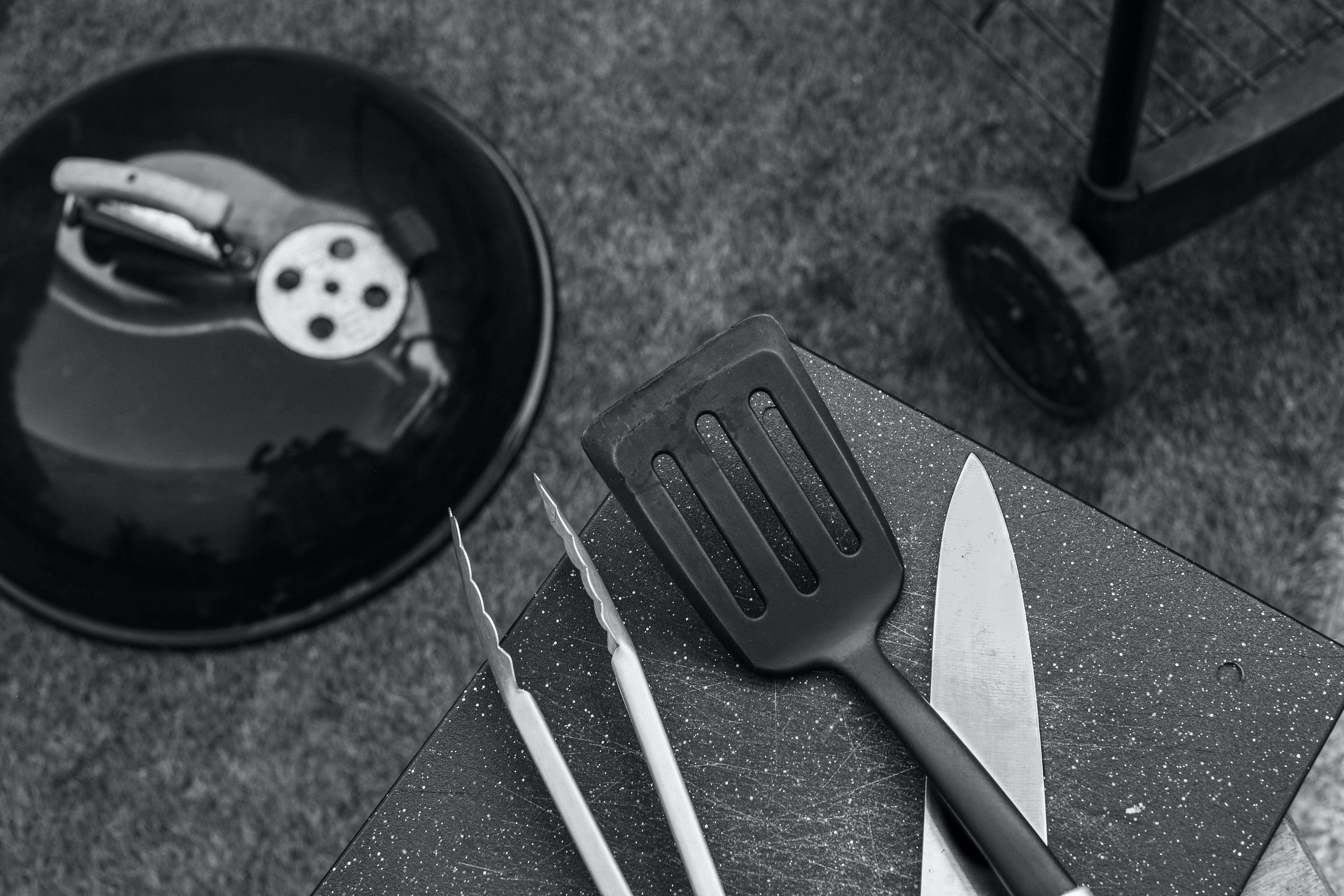 A spatula, tongs, and a knife near a grill.