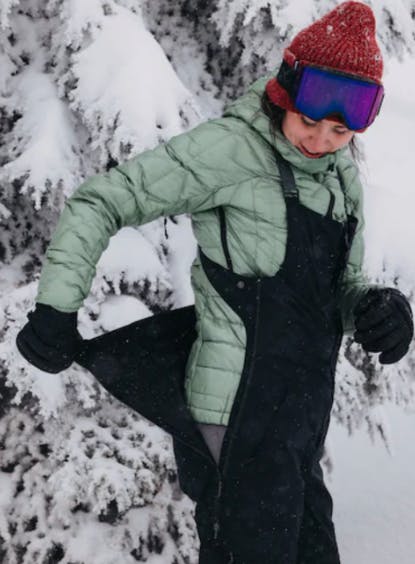 A skier in the Burton Women's GORE-TEX 2L Kimmy Bib Pants - Tall looking at the side zipper.