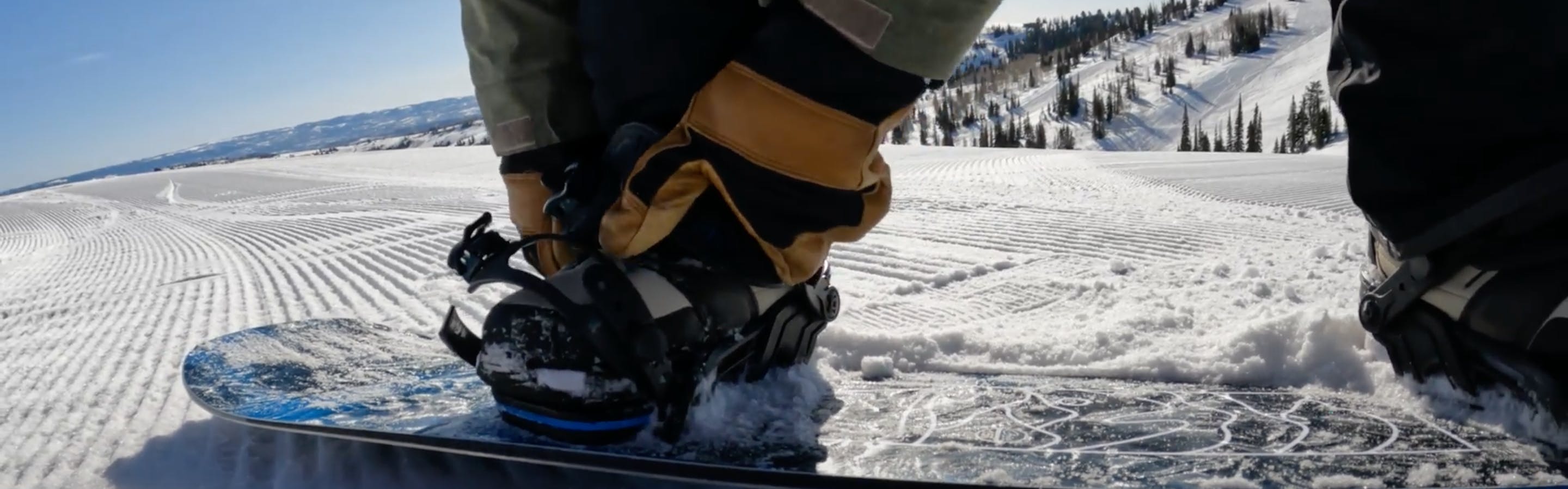 A snowboarder strapping into a snowboard. 