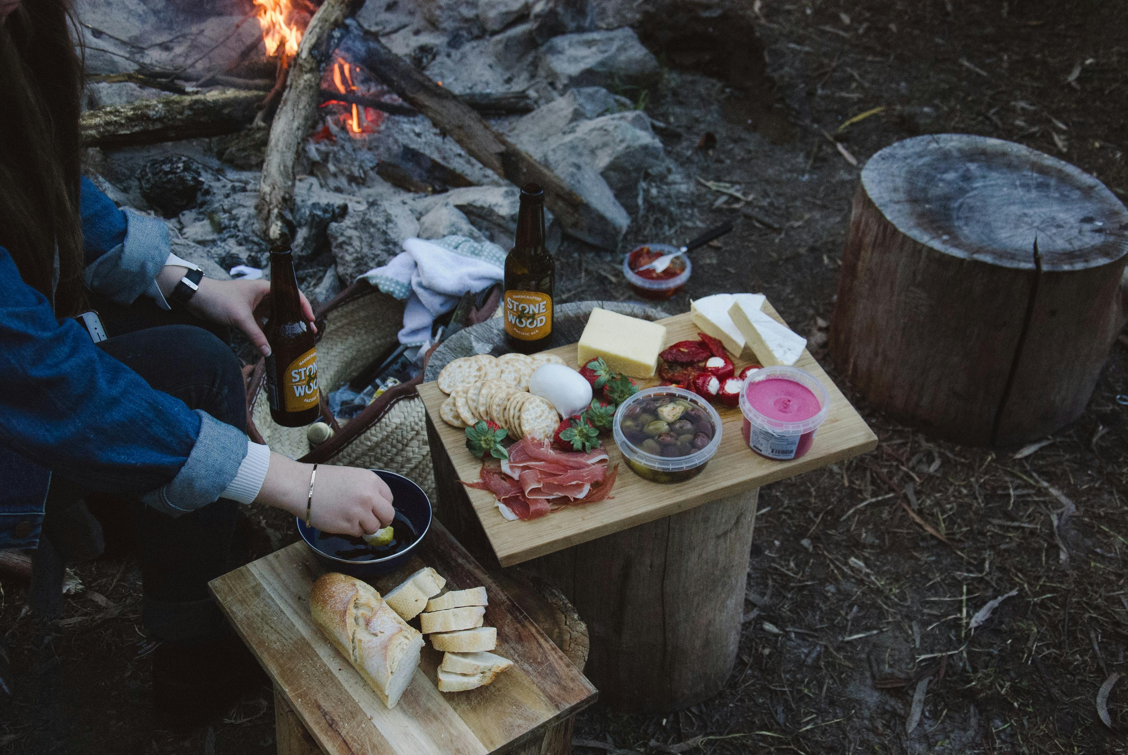 A camper eating something off a charcuterie board. There is a campfire in the background. 