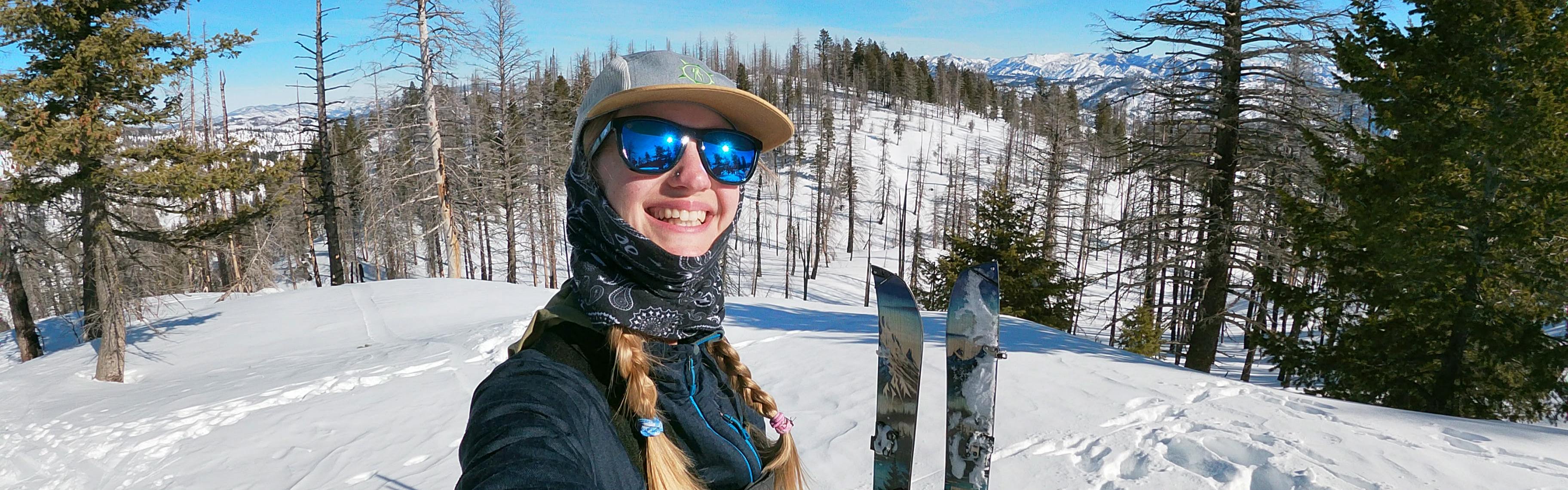 A selfie of a splitboarder with the Jones Frontier Splitboard sticking in the snow behind her. 