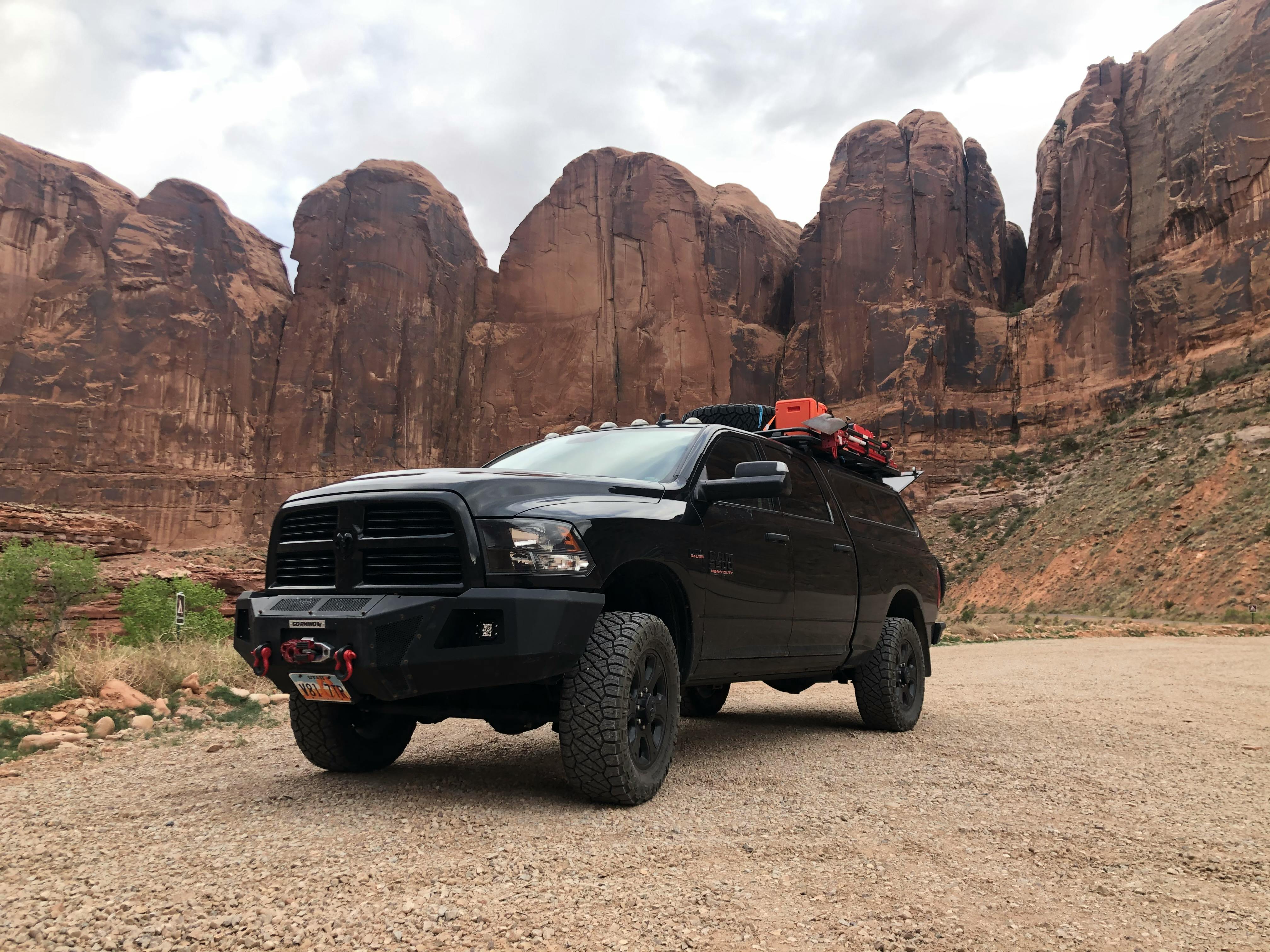 A black truck in front of some red rocks.