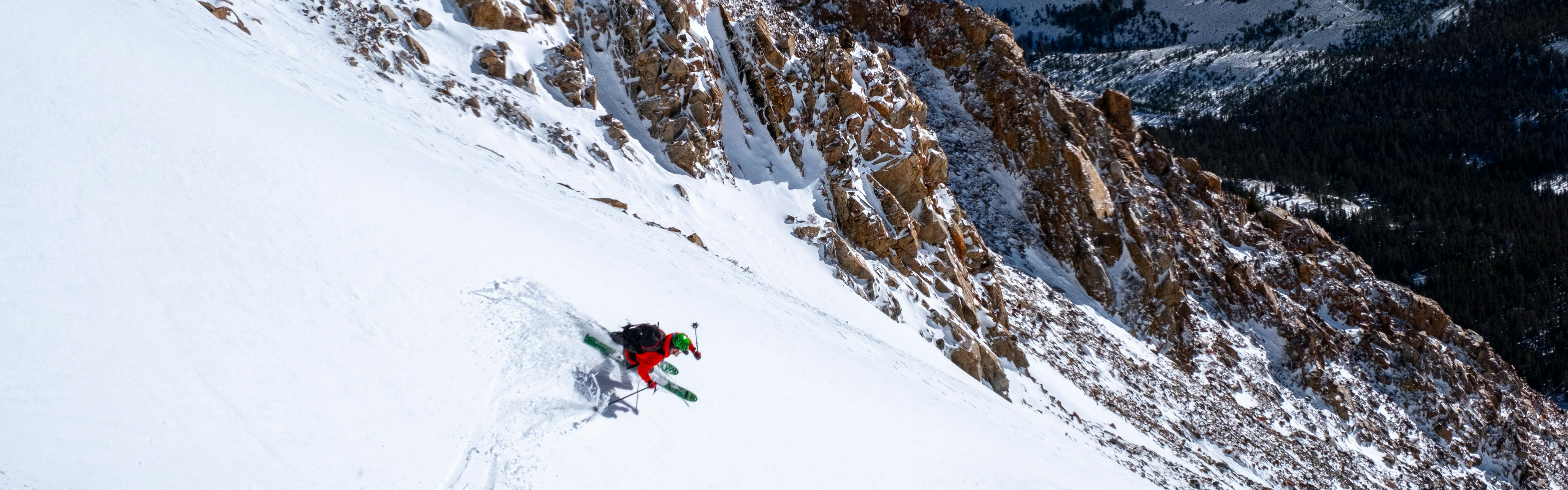 skiier in red jacket descending steep hill in powder