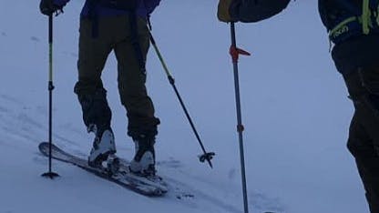 Two people with backcountry ski gear walk up a mountain.