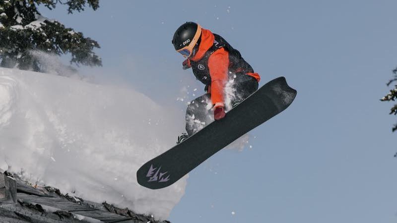 A snowboarder comes off a man-made jump and grabs the bottom of their board.