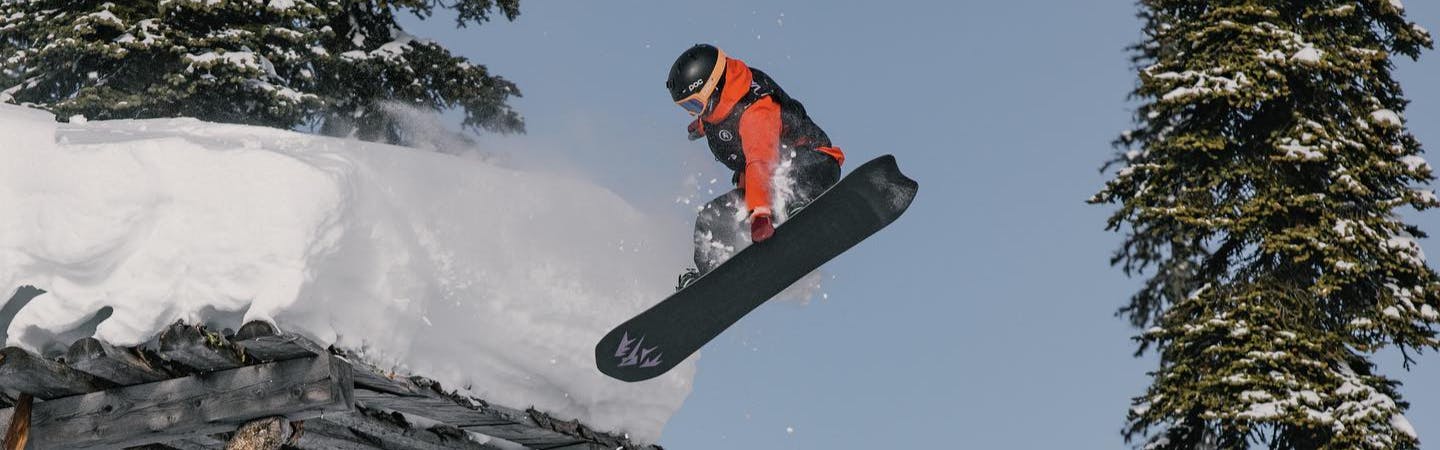 A snowboarder comes off a man-made jump and grabs the bottom of their board.