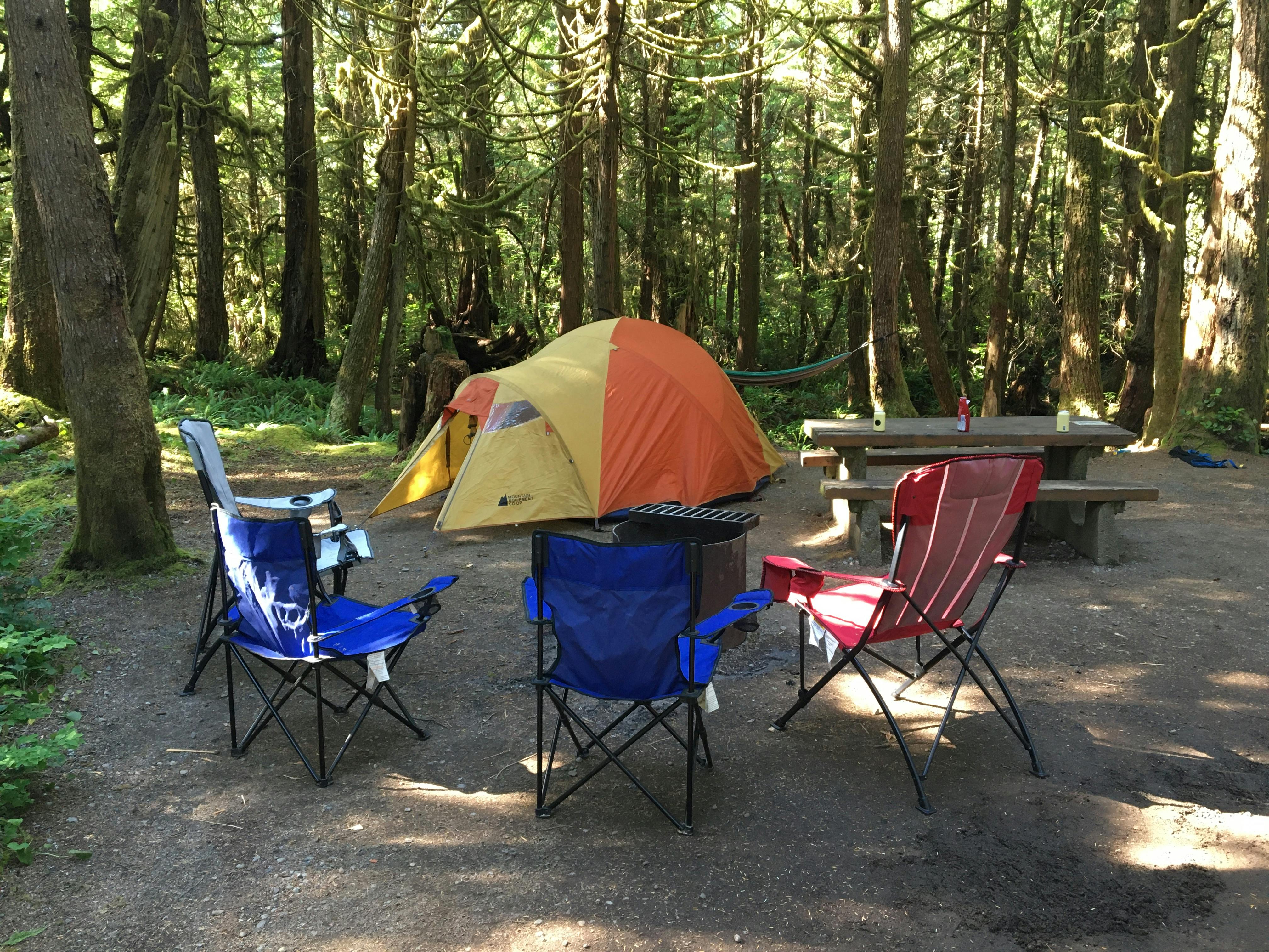 Four camp chairs sit in a ring around a fire pit with a tent in the background