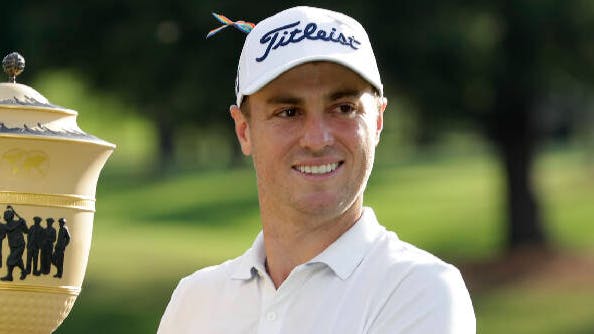 Justin Thomas holds up a large trophy while wearing a Titleist hat. 