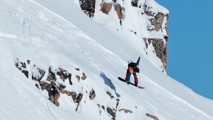 A snowboarder jumps off a natural rocky ramp and grabs his board at Kicking Horse, BC in the 2020 FWT. 