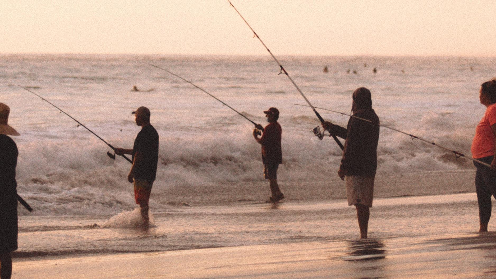 Five anglers stand in the waves and fish on the sea.