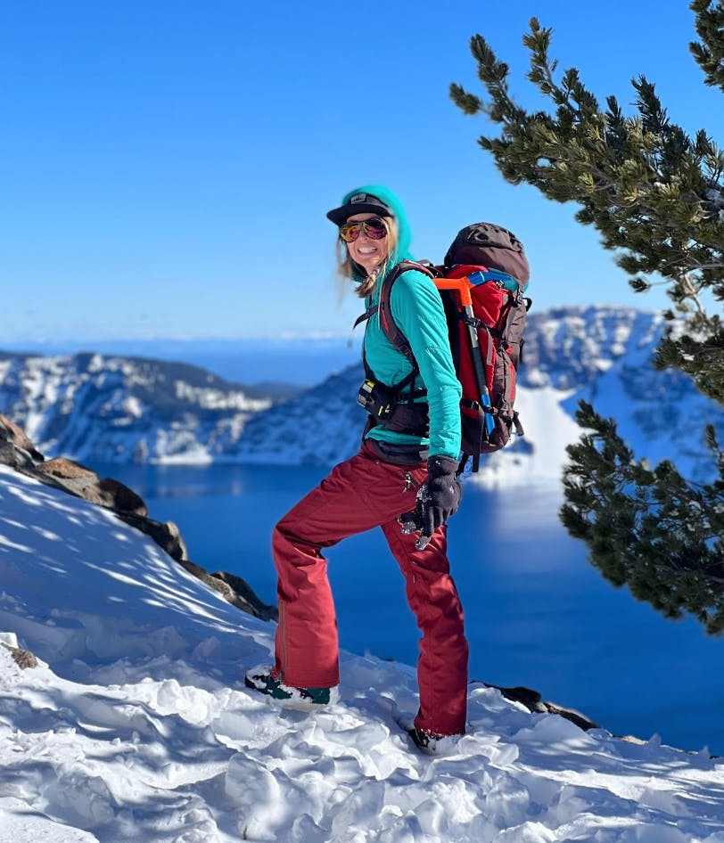 A snowboarder standing at the top of a snowy run with a lake in the background. 