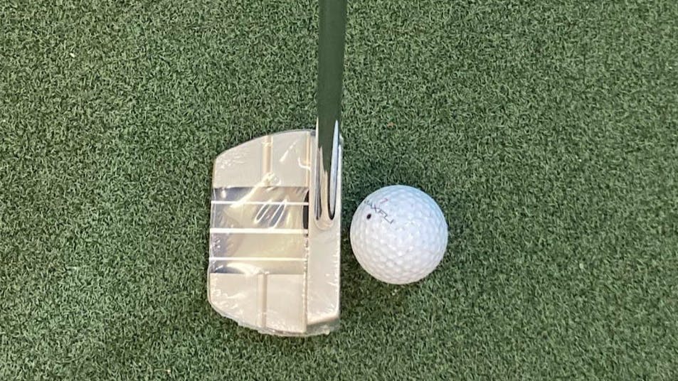 The Cleveland HB Soft Milled #10.5 Center Shaft Putter in front of a golf club.