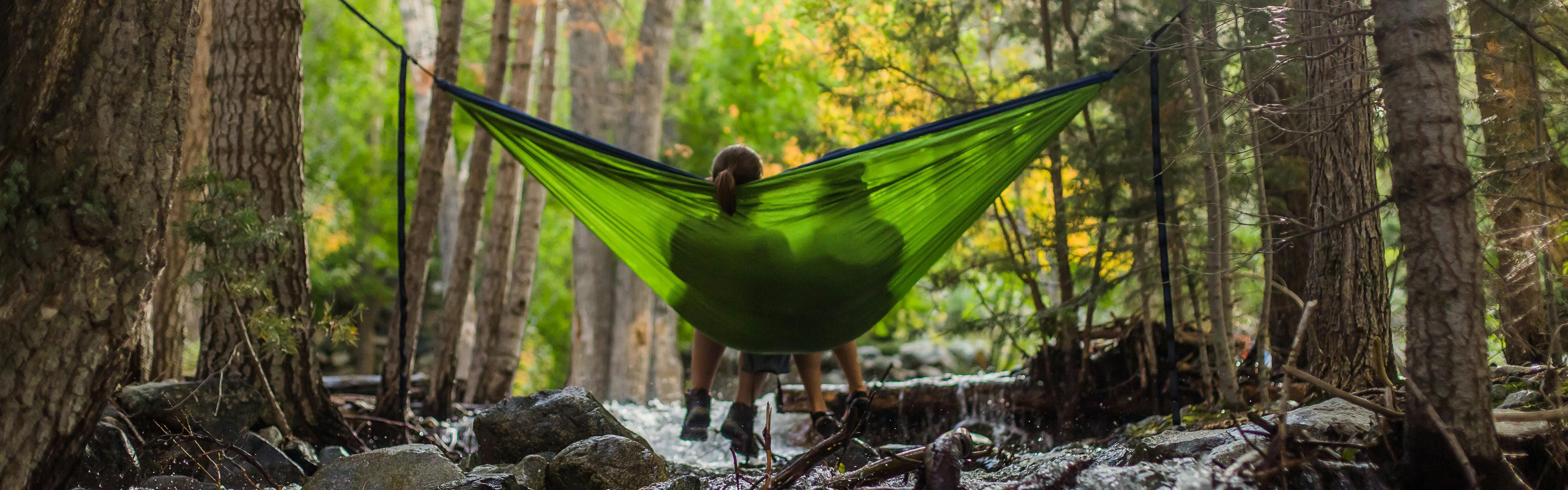 Two people sit in a green hammock in the forest