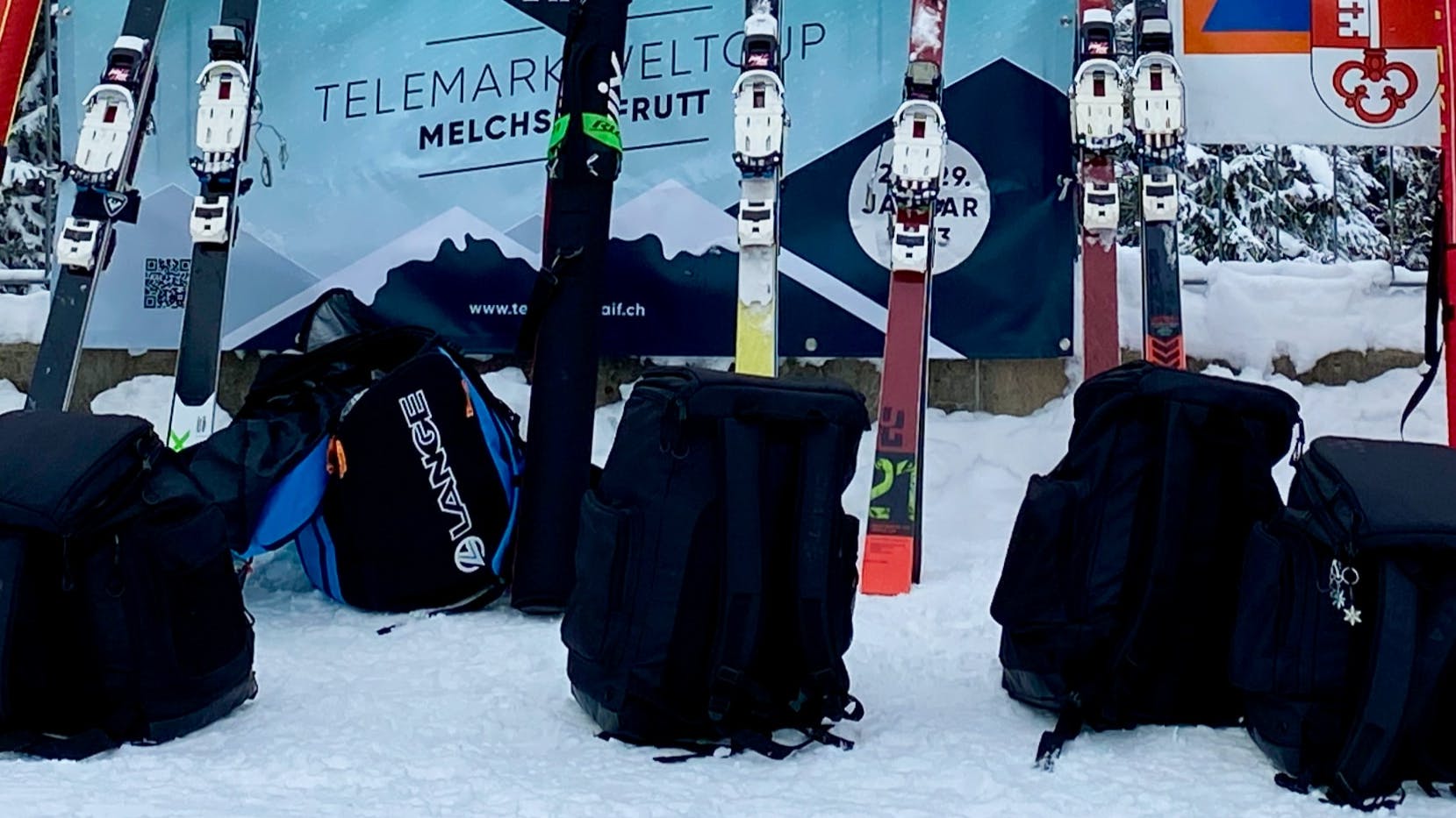 Several pairs of skis and ski boot bags in the snow. 