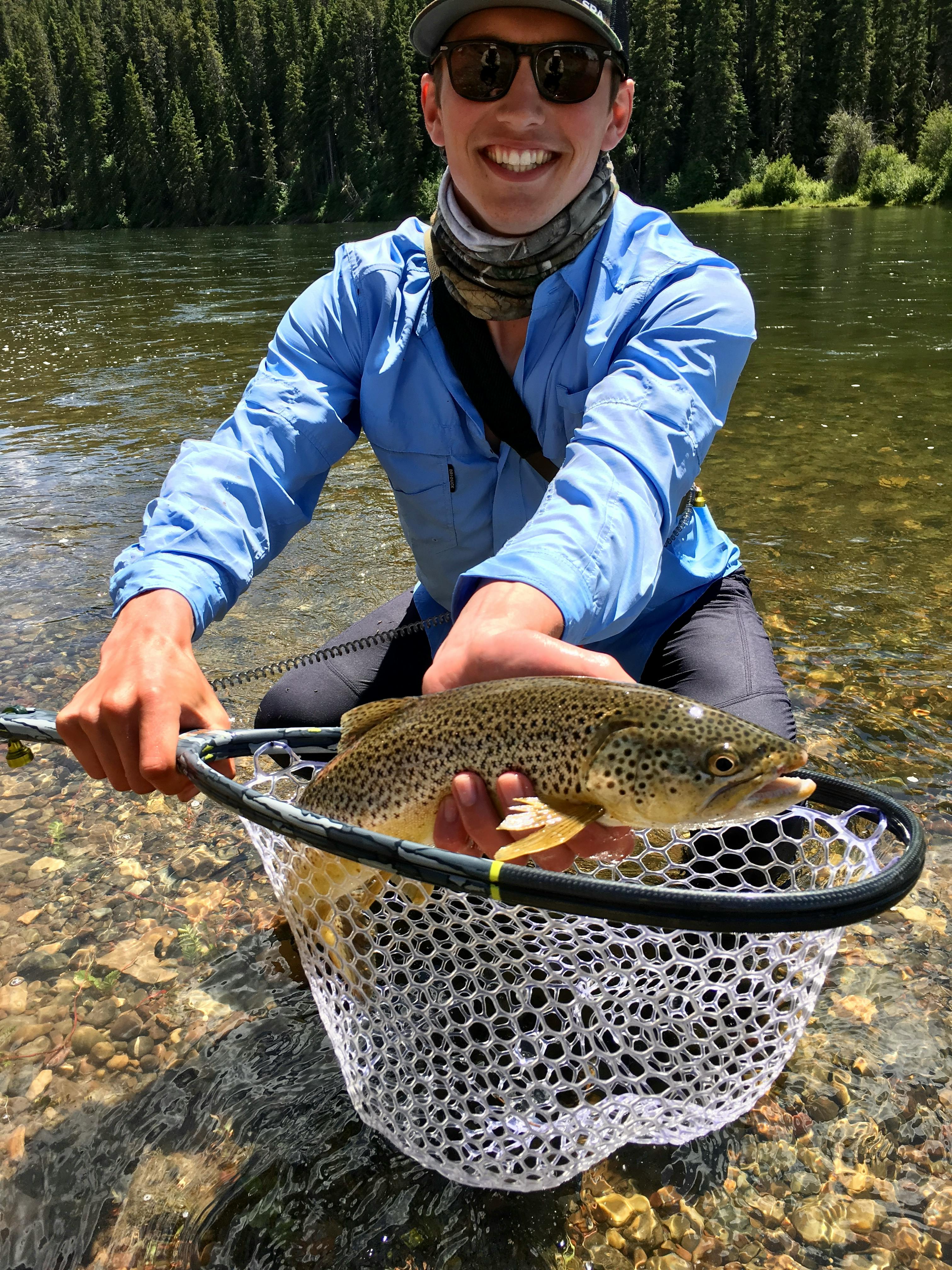 Curated expert Auggie Lange crouching in the river holding up a fish over his net