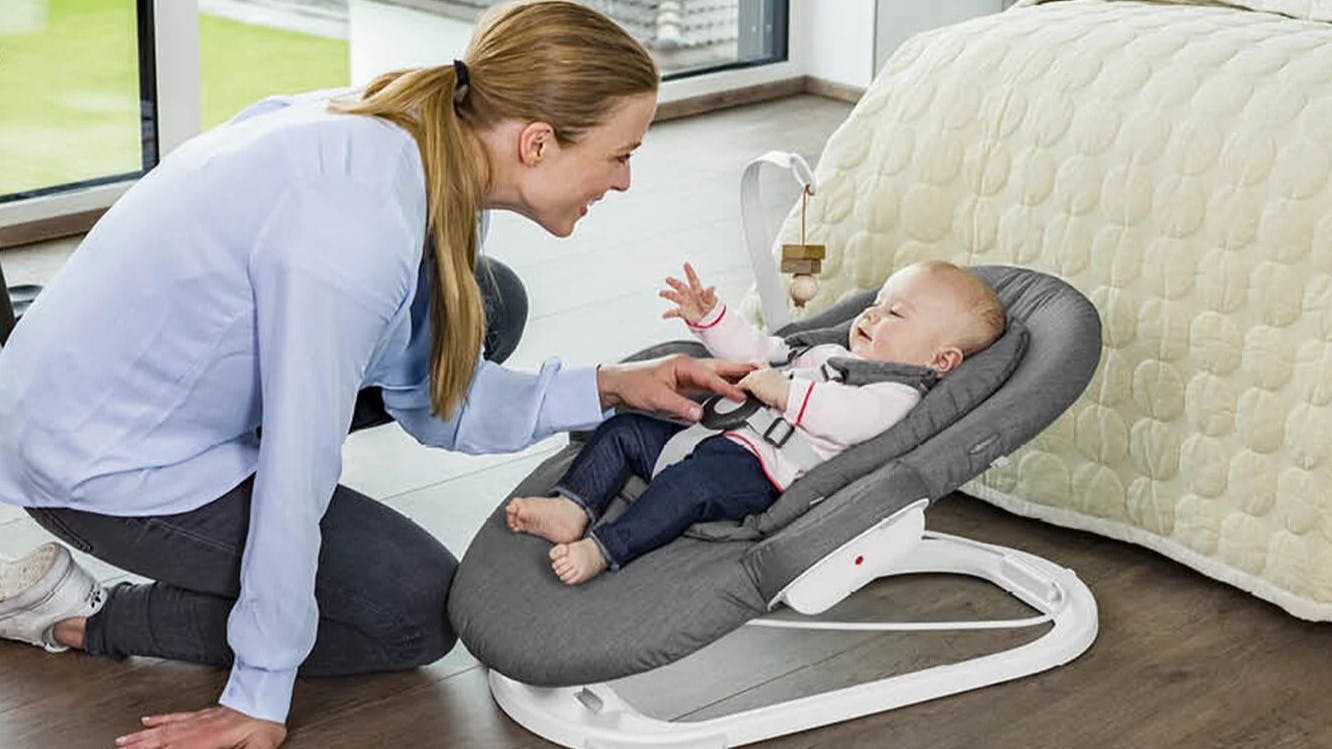A mom smiles at a baby in a bouncer.