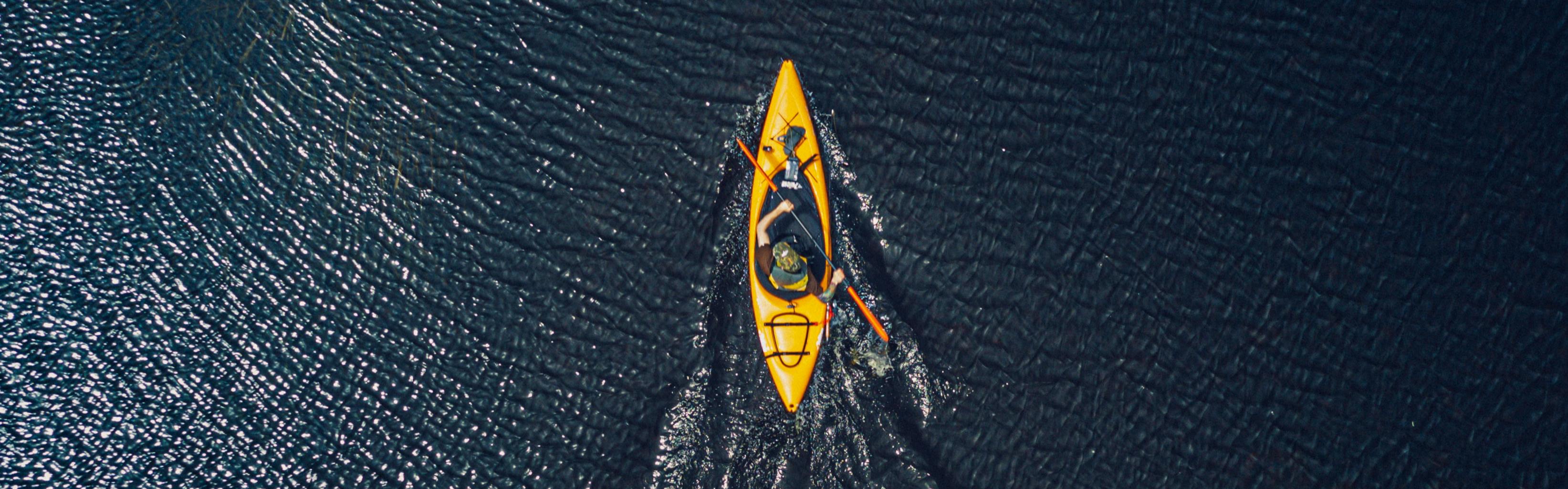 The photo is taken from above and looks down on a man kayaking in dark blue water.