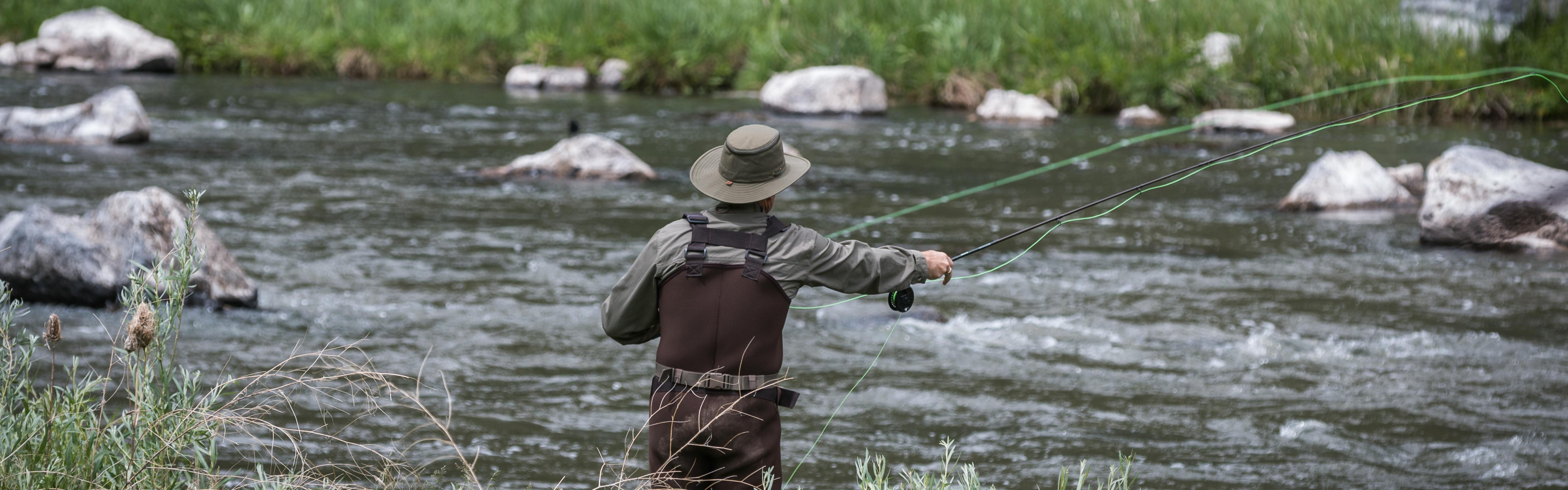 A man is fly fishing and standing in a river with waders on. 