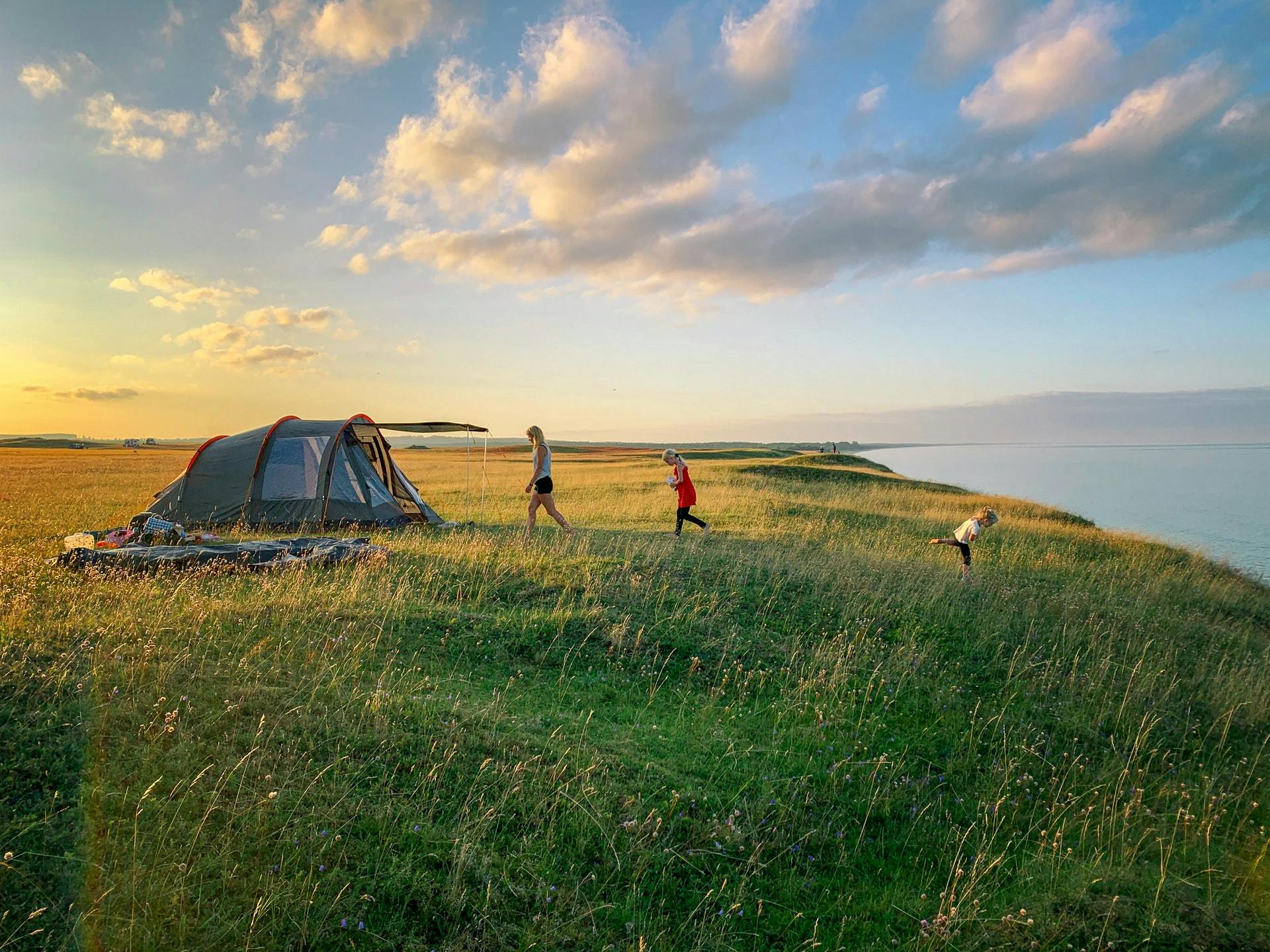 Three people running near a tent that is pitched in an open plain.