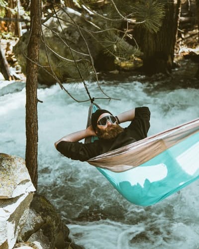 A man lounges in a hammock suspended over a river
