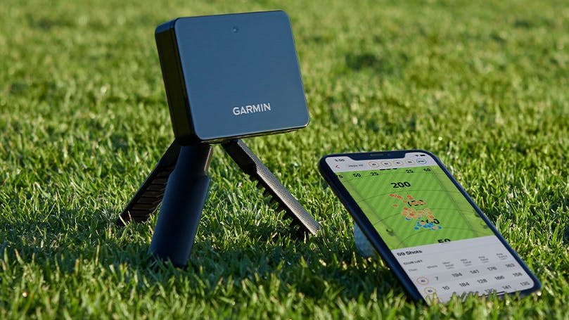Garmin R10 sits on some grass near a phone.