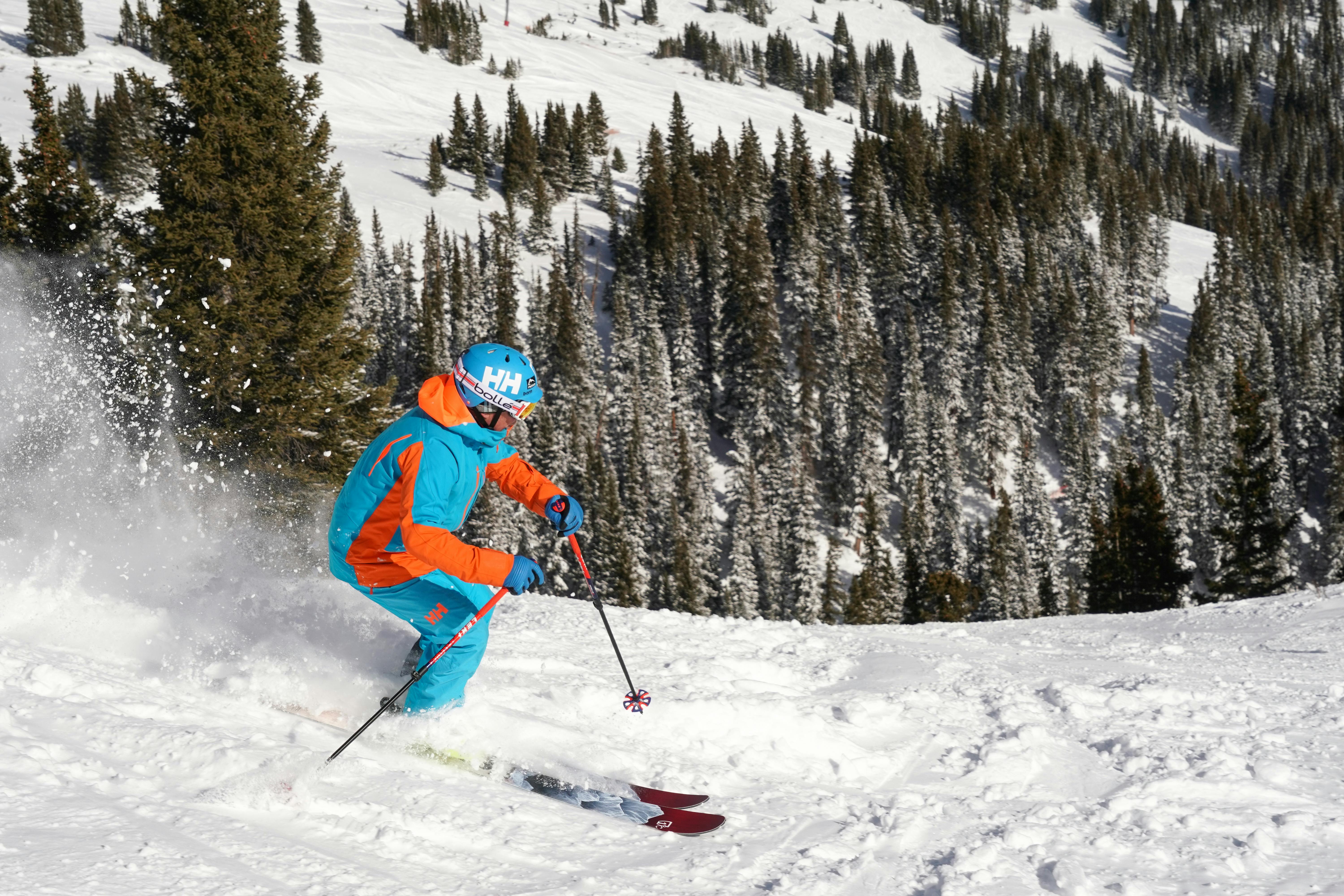 A man in a blue and orange ski jacket and pants ready to ski down a slope