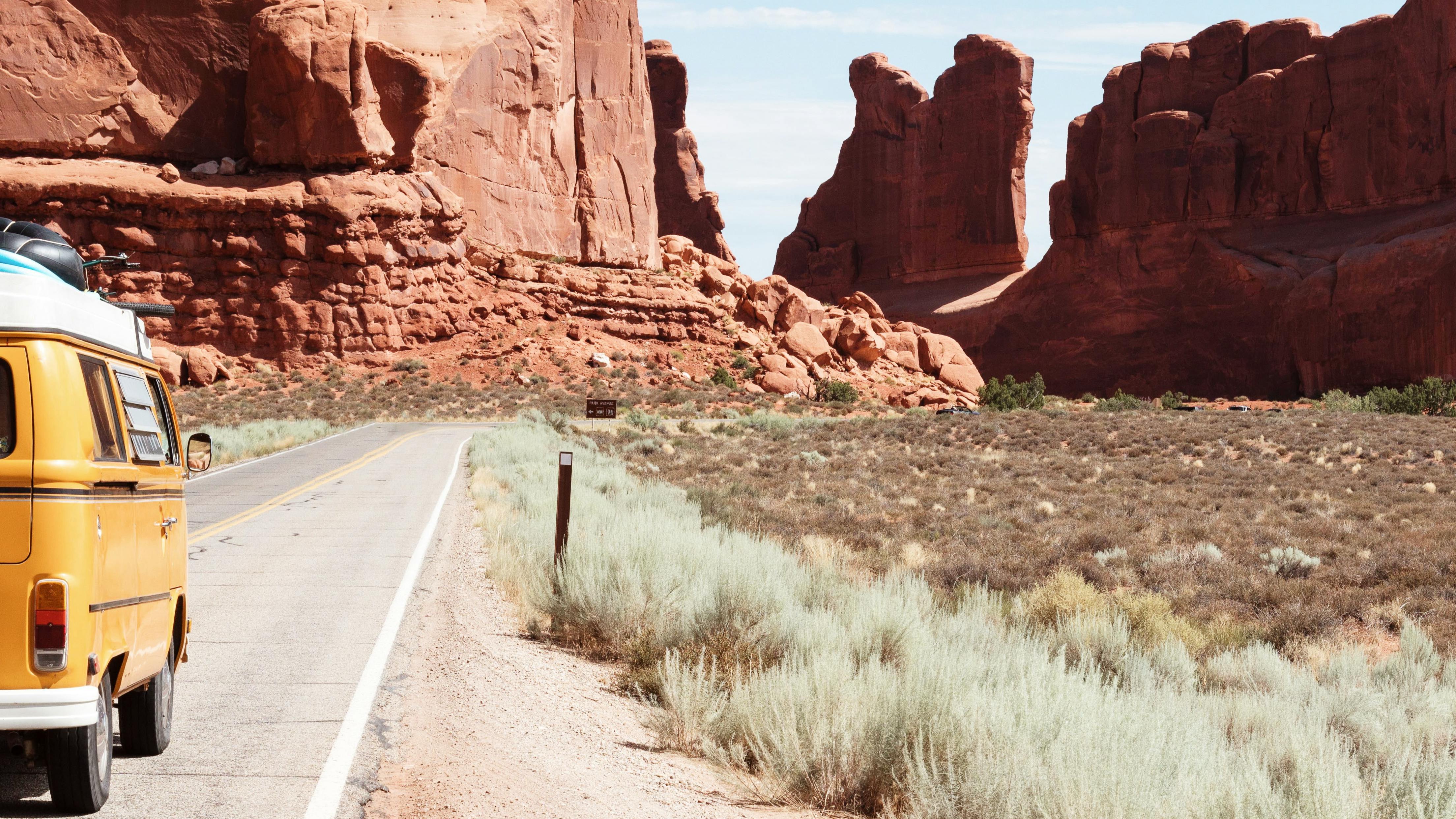 An orange van drives in a red rock canyon.