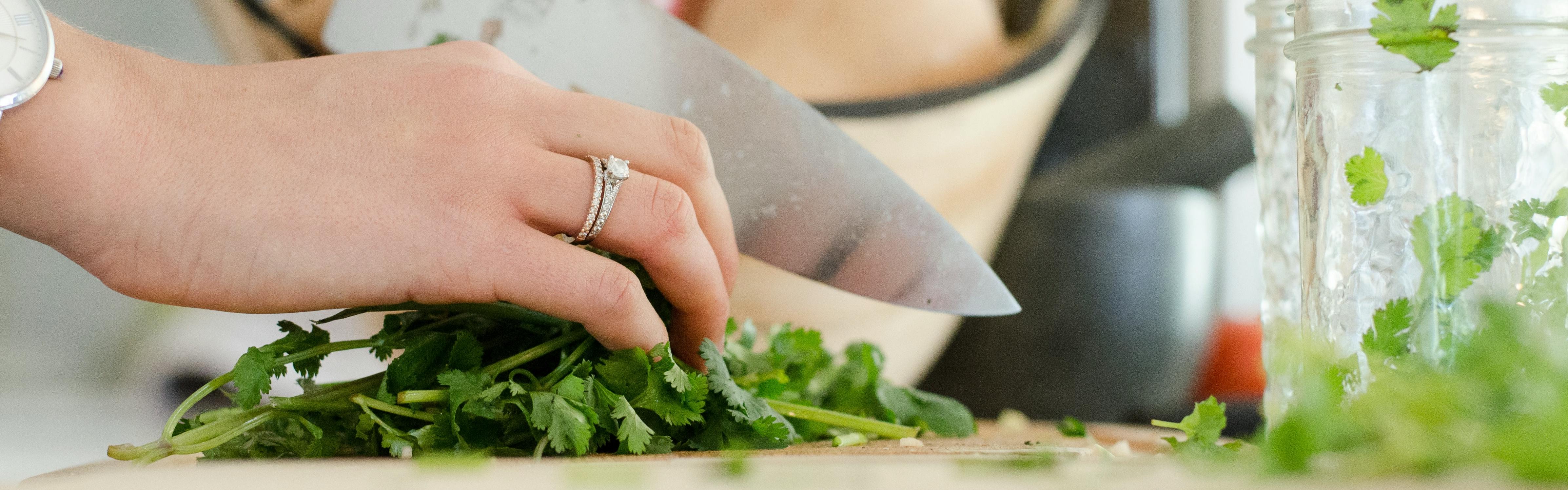 Close up of a woman's hand cutting herbs with a sharp knife.
