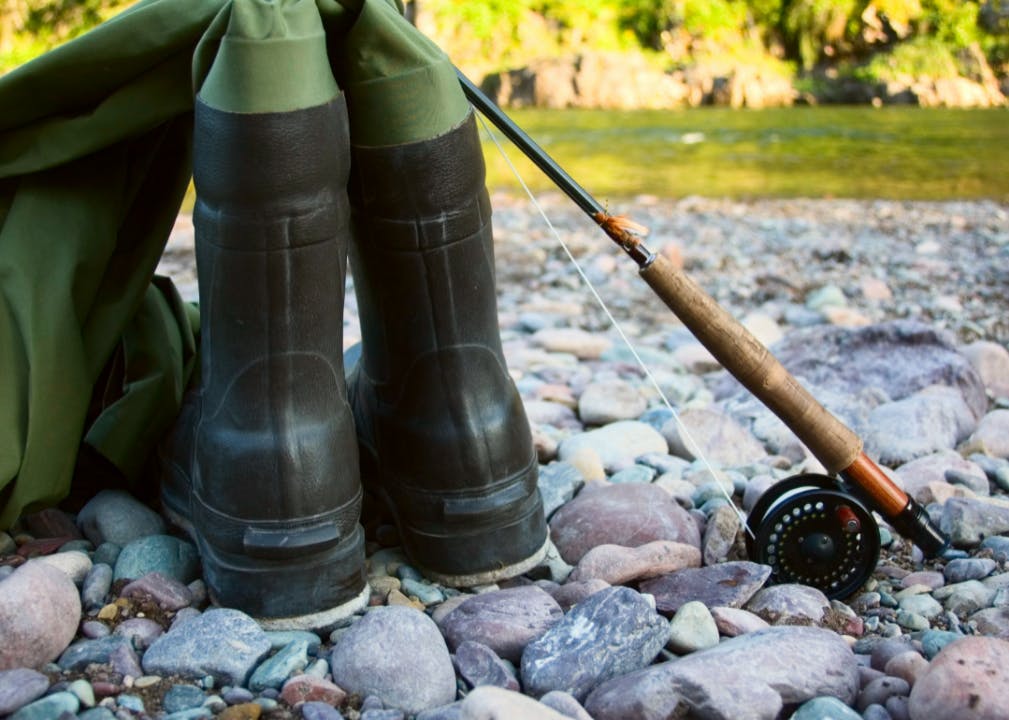 A fly rod leaning against a pair of waders on a rocky river bank