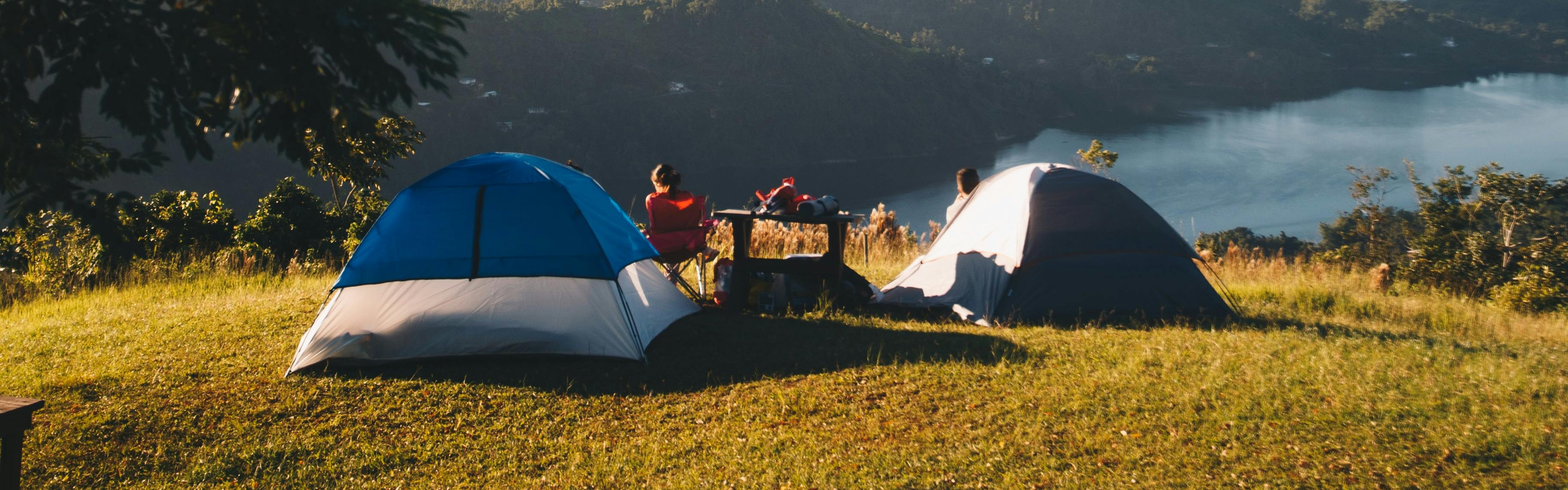 Two tents are set up on a grassy hill with people sitting at a set of tables outside them