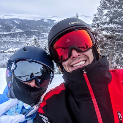 Selfie of two skiers wearing helmets, goggles, and jackets. 