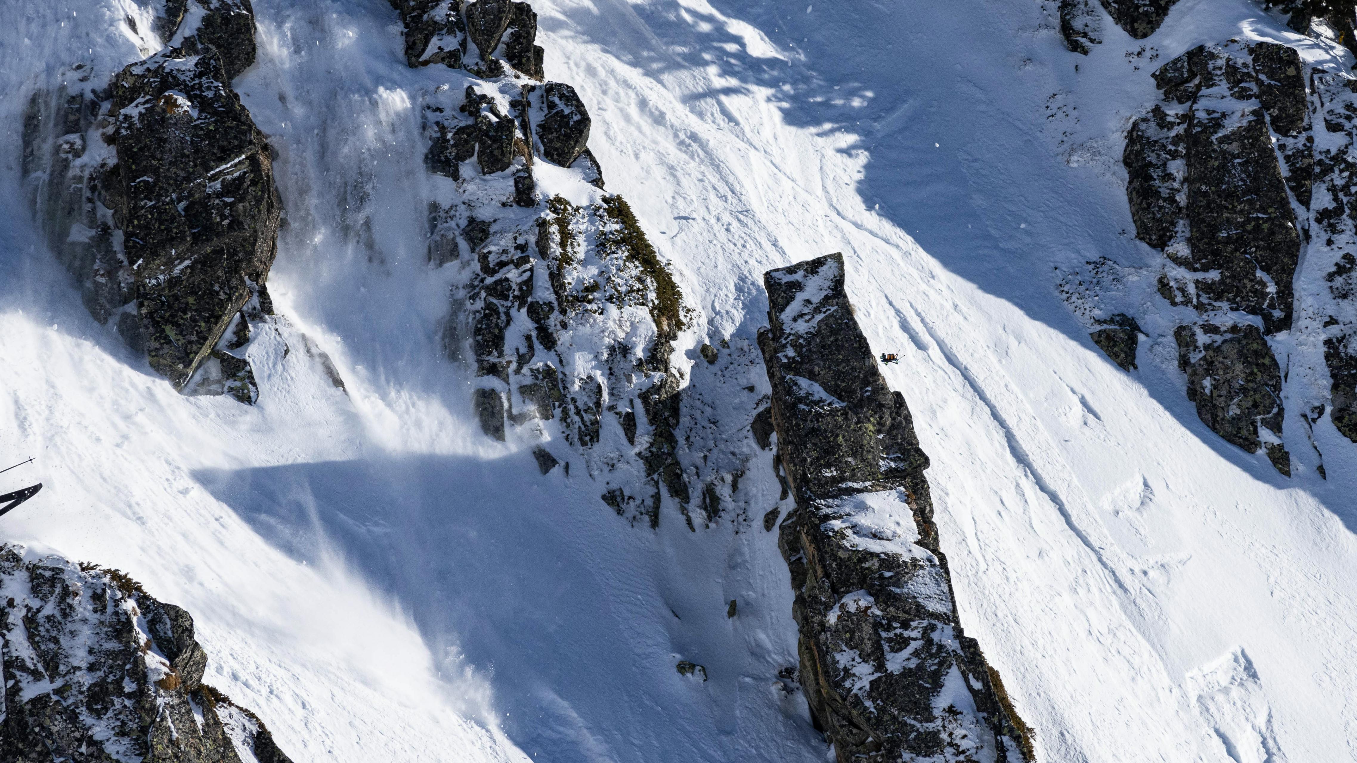 A skier jumps while on a near-vertical mountain.