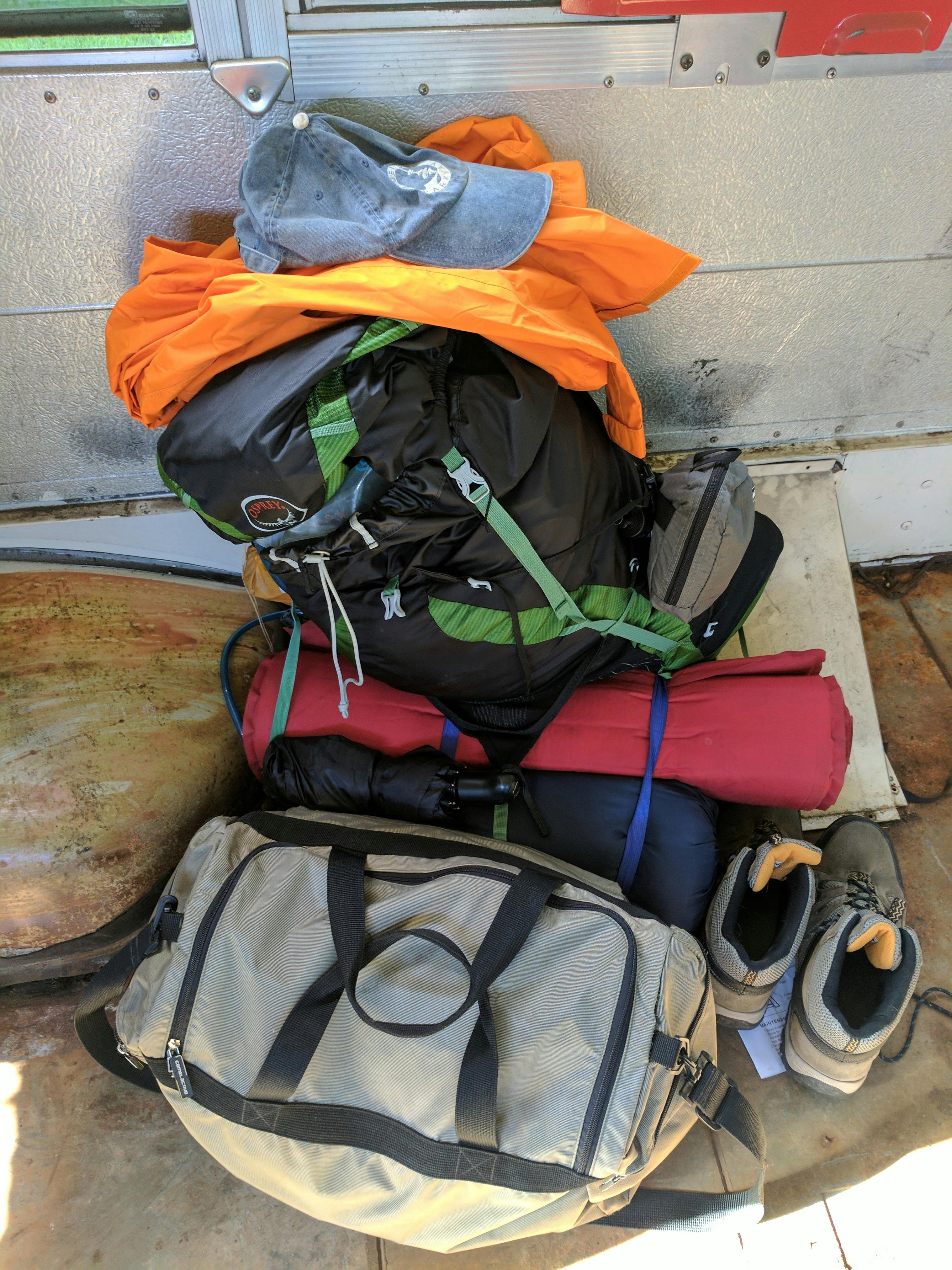 A backpack, some hiking shoes, a hat, and some other gear in a pile.