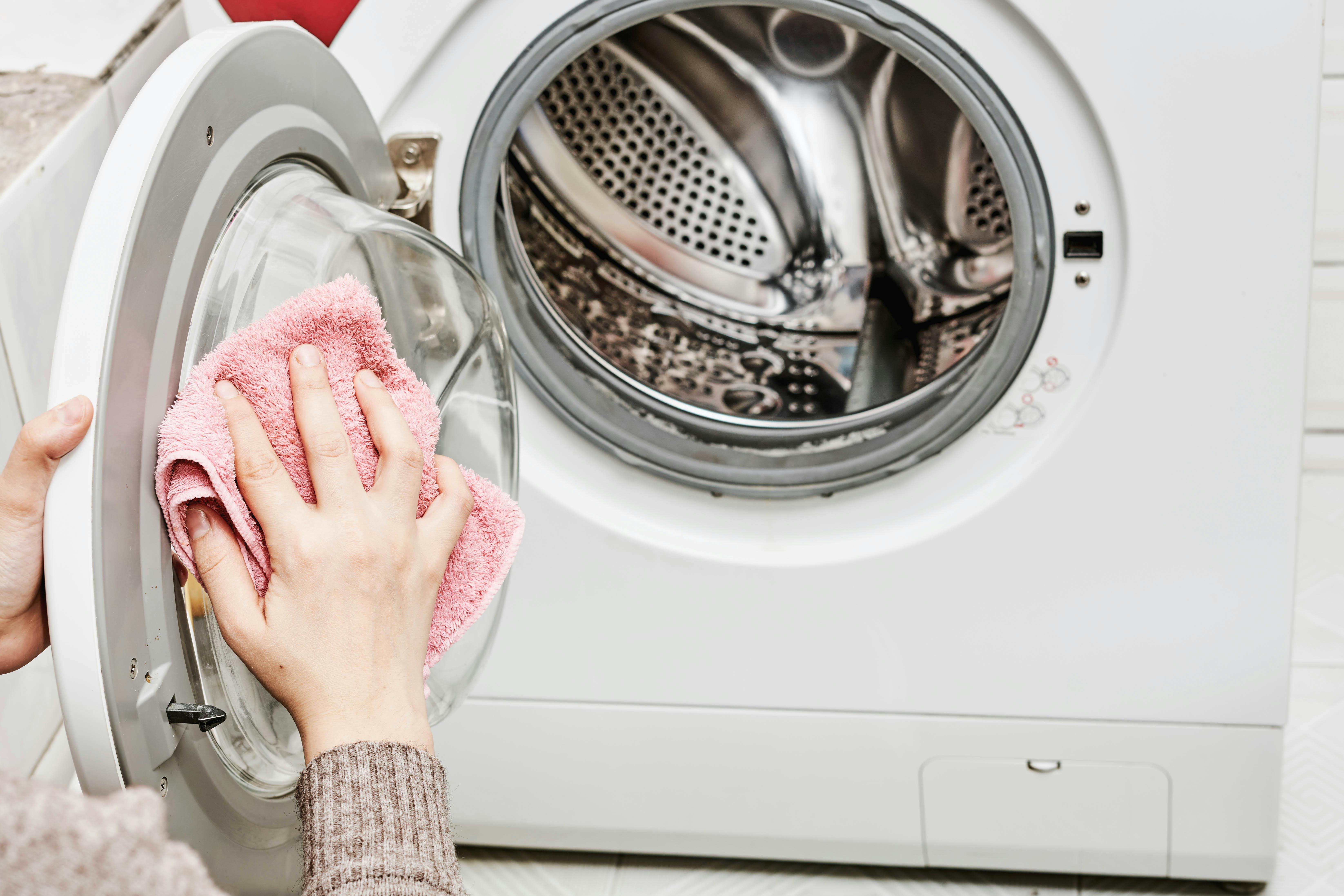 A woman wipes down her washing machine with a cloth.