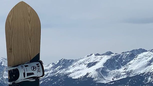 The Nidecker Mellow Snowboard · 2022 with a snowy mountain range in the background. 