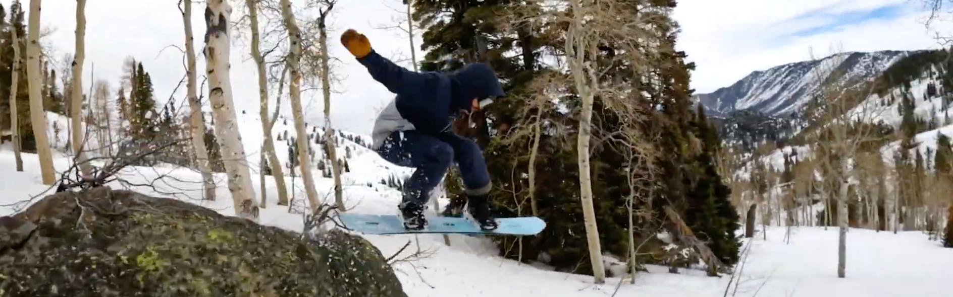 Snowboard Expert Matthew Kaminski jumping off a boulder with the 2023 K2 Passport snowboard